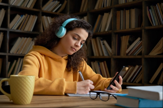 Jovem de fone de ouvido em biblioteca estudando e cronometrando exercícios de prova